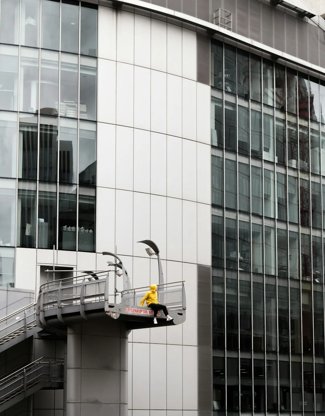 services-02 Black and white from below of man steeplejack in protective helmet with professional equipment cleaning glass wall of modern tower